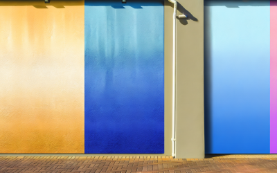 Couleur en I : Un mur de maison peint avec un dégradé de différentes nuances commençant par la lettre I : ivoire en haut, indigo au milieu et bleu glace en bas. Effets d'ombre et de texture pour un rendu réaliste, éclairage pour un effet ensoleillé. Mur en focus avec flou artistique sur les éléments environnants.